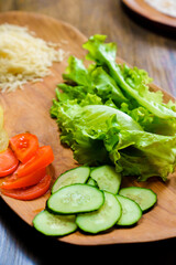 lettuce, ringed tomato and cucumber on a wooden cutting board.