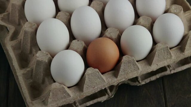 man put brown egg in cartboard box to white eggs