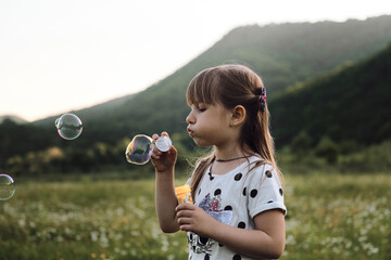 Happy childhood in nature among flowers. Chamomile field and child at sunset. Little girl in dress...