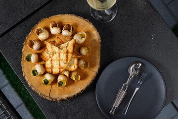 Baked snails with garlic oil and herbs on a wooden plank