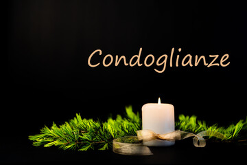 Scena con una candela bianca accesa circondata da rami di abete con la scritta condoglianze su sfondo nero. Commemorazione. Lutto. Anniversario.
