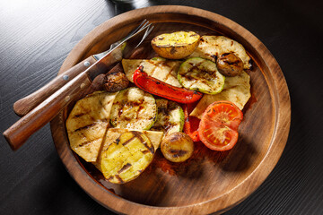 set of baked vegetables zucchini tomato potatoes bell pepper on wooden plate