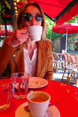 Woman on a terrace with a cup of coffee or tea, relaxing in the sun. Street blurred deliberately in...