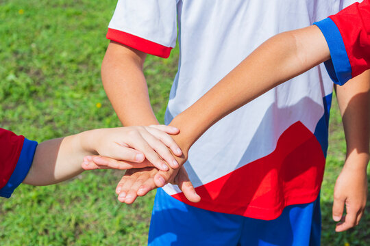 A close-up of the cropped hands of young soccer players. Children shake, put their palms on top of each other. Team unity and desire to win.