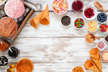 Summer ice cream buffet with a variety of ice cream flavors and sweet toppings. Above view frame over a rustic white wood background.