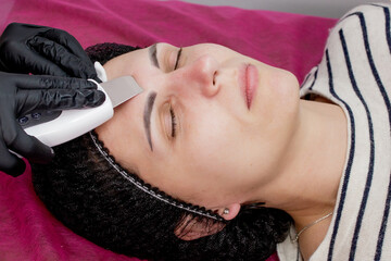 Cosmetologist,beautician making facial treatment with ultrasonic spatula to young woman,face skin...