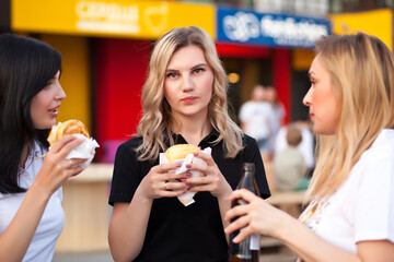 Pretty young women eating hamburger outdoor on the street