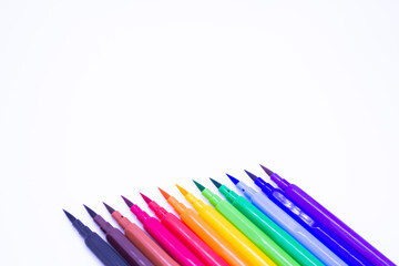 Multi-colored markers with a brush tip, arranged according to the colors of the rainbow. White background. The concept of creativity, drawing, bright world, back to school, study. Copy space