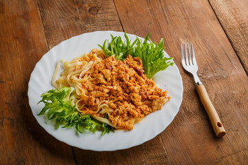 A plate of bolognese pasta decorated with herbs on a wooden table next to a fork.