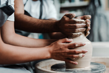 Photo near and side. Male and female hands make a vase of clay. Date in the workshop