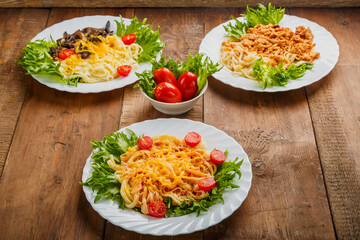 Three plates with different pasta on a wooden table near salted tomatoes.