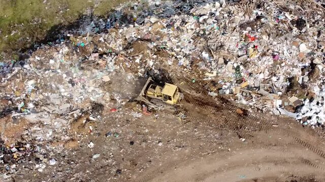 Large city trash can. Waste disposal site. An old tractor pushes a lot of debris. A huge pile of rubbish. The video was filmed from a drone.