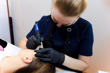 the master of permanent makeup sitting in the cosmetology office and bending over the client...