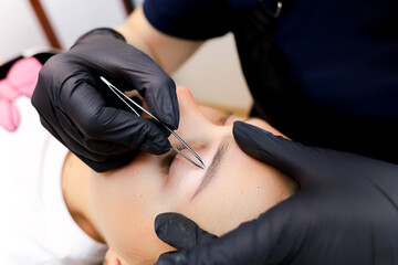 the permanent makeup master performs plucking of unnecessary hairs in the eyebrow area after the...