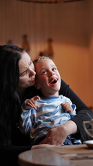 Close up portrait of a little boy with special needs and mom laughing at a table in a cafe,...