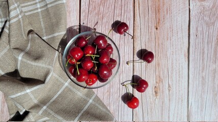 View on top of sweet red cherries in bowl and brown napkin on the side, selective focus, copy space. Sunlight coming over the table, shadows. Eating fruits outside in summer day. Raw images, unedited.