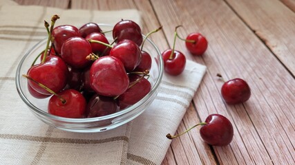 View on top of sweet red cherries in bowl and white napkin on the side, selective focus, copy space. Sunlight coming over the table, shadows. Eating fruits outside. Unedited. Copy space available.