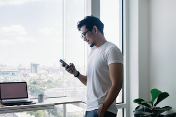Happy Asian man using smartphone with balcony view. Concept work from home.
