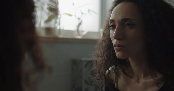An insecure young woman staring at her reflection in the mirror, feeling lonely and sad. Slow motion, handheld, close up. 