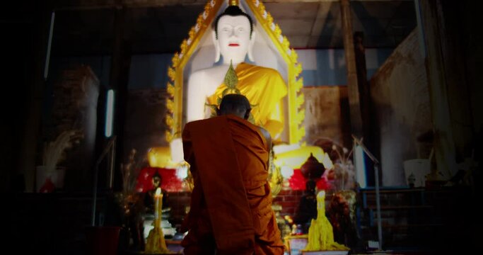A back view slow motion of Buddhist monk kneels and pays homage to the Buddha three times in a very old church.