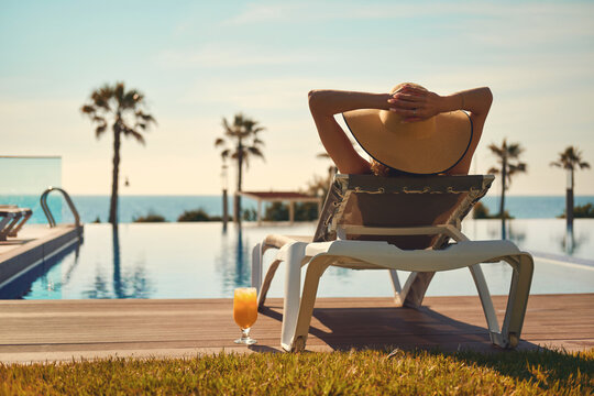 Rear view woman wear hat sunbathing on deckchair on poolside