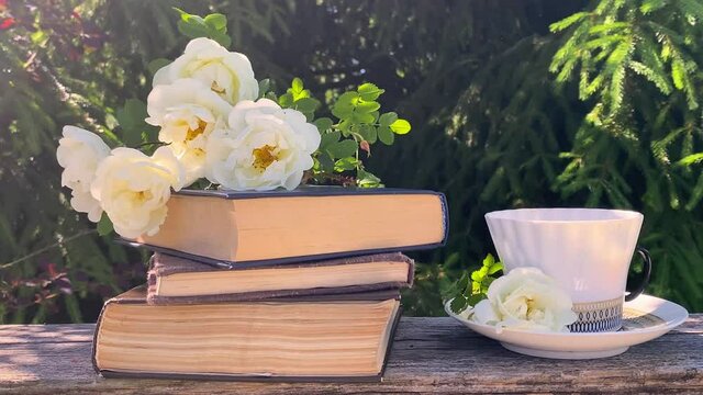 Beautiful summer composition  - cup of coffee, bouquet of white rose hips flowers and books on a natural green background, a concept of good morning, summer mood, happiness