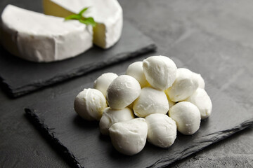 Mozzarella cheese balls and camembert on black slate board over dark concrete background