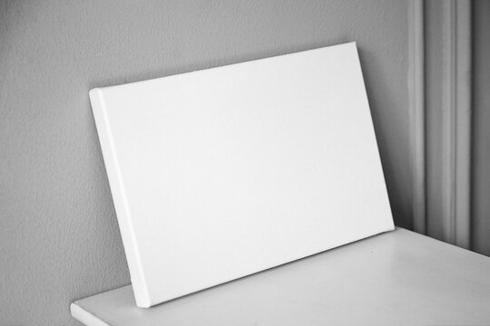 White canvas mockup, blank picture on wooden table in interior with grey wall