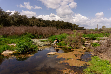 young man sitting on a rock in the river at mountains