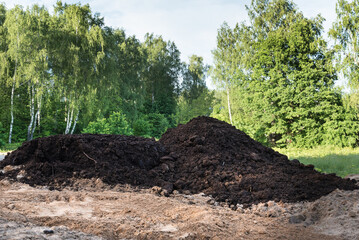 A large pile of black earth. Fertile land against a background of green trees