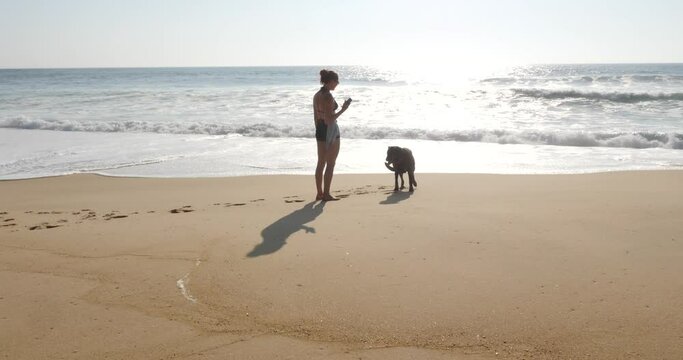 beautiful young woman taking photos of her dog on the sunny beach