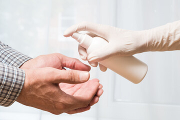 A woman wearing medical gloves applies an antibacterial spray on a man's hands. Protection against infection.