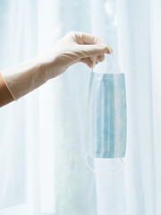 A woman's gloved hand holds a medical mask. Protection against infection.