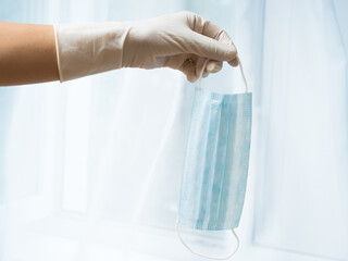 A woman's gloved hand holds a medical mask. Protection against infection.