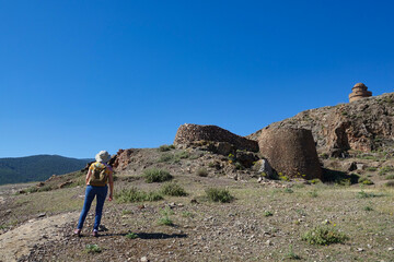 Fototapeta premium Woman with hat and small backpack going up a hill towards the medieval castle of La Calahorra (Granada, Spain) on a sunny spring day