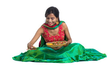 Portrait of a Indian Traditional Girl holding Diya and making Rangoli. Girl Celebrating Diwali or...