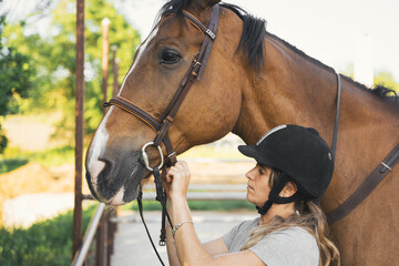 Equestrian sporty female putting bridle on horse
