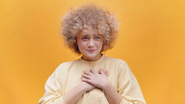 Sweet Young Girl With Both Hands On Her Heart As If Expressing Gratitude. Positive Emotions. Dressed In A Baggy Yellow Sweater. Lifestyle Concept. 