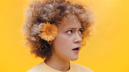 Beautiful girl with a flower on her ear looking dissatisfied. Unhappy girl showing her dislike for...