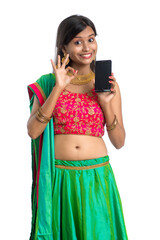 Young Indian traditional girl using a mobile phone or smartphone and showing blank screen smart phone on white background