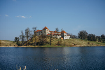 Fototapeta na wymiar Panorama of a beautiful ancient castle with brown tiles on the shores of lake. Fortress on the mountain near the beautiful spring lake.