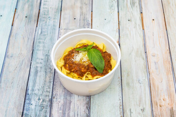 Bowl of noodles with bolognese sauce, cheese and basil in home delivery container