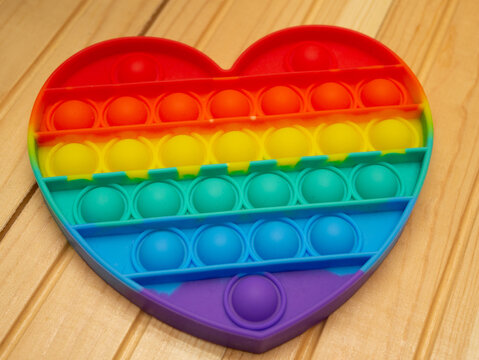 Colorful trendy Pop it fidgets heart shape toy on wooden background. Toy anti-stress, simple dimple. 