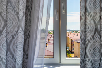 View from a window with gray curtains ajar on houses and roofs of buildings. Intimate secrets of...
