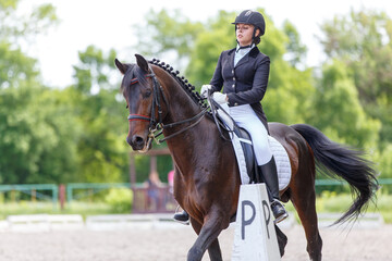 Young sportswoman riding horse on advanced dressage test during the equestrian competition