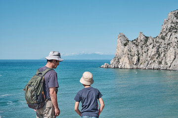 A boy and his grandfather standing on the shore of the bay, talking, looking at the rock.