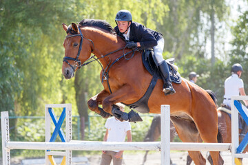 Young rider man jumping over the barrier