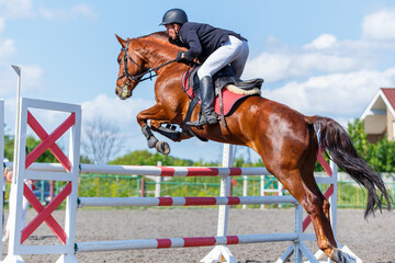 Young rider man jumping over the barrier