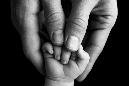 Father holding newborn baby's fingersnewborn . Hand of a newborn baby. Hands of parents and baby closeup. Black studio background. Black and white photo. 