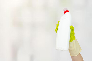 Spring cleaning concept. White bottle with liquid detergent in hand with yellow rubber gloves. The concept of cleaning service.